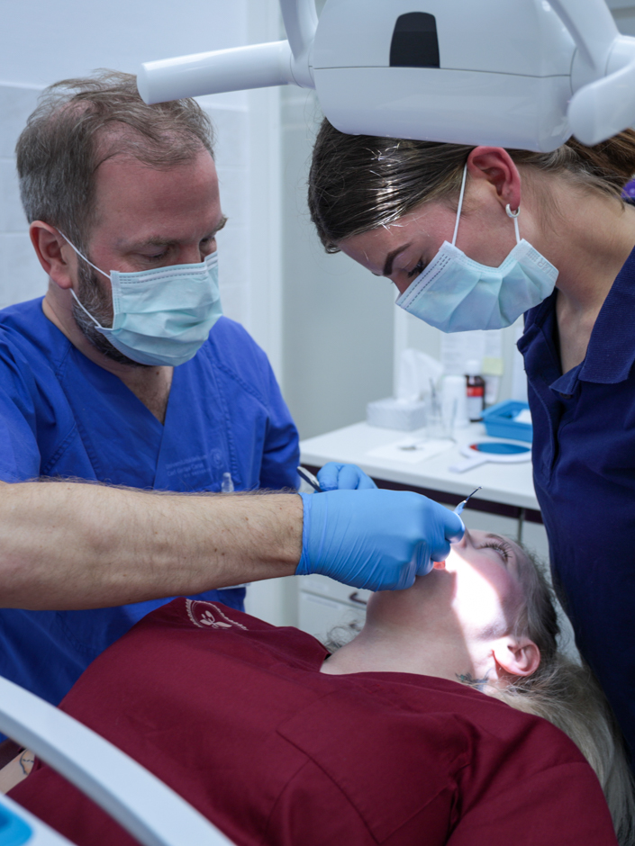 Zwei Zahnärztinnen behandeln eine Patientin auf dem Zahnarztstuhl. Einer führt das Instrument, die andere schaut zu.