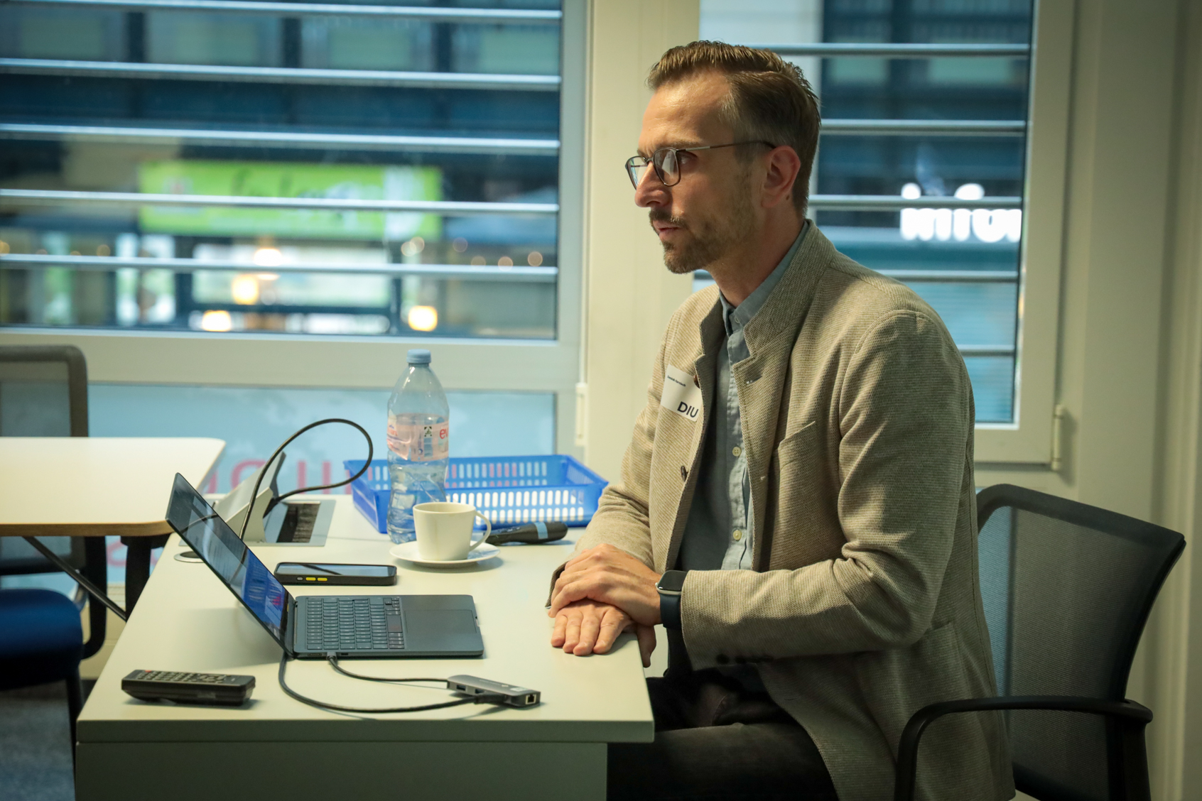 Mann mit Brille und grauem Sakko sitzt an einem Tisch vor einem Laptop.