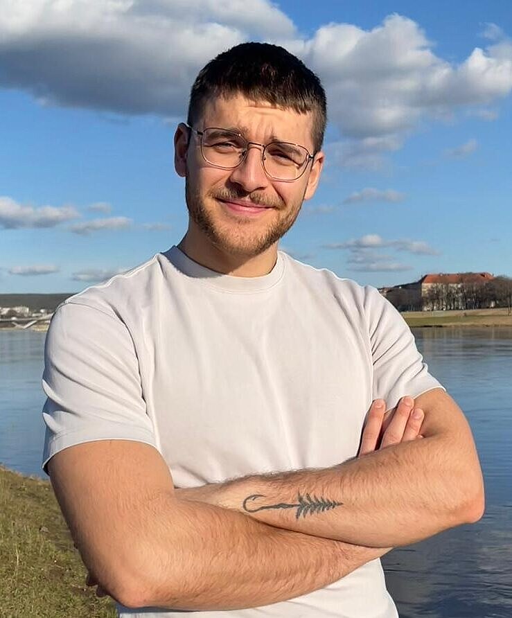 Physiotherapeut Jan steht mit verkreuzten Armen vor einem Fluss.