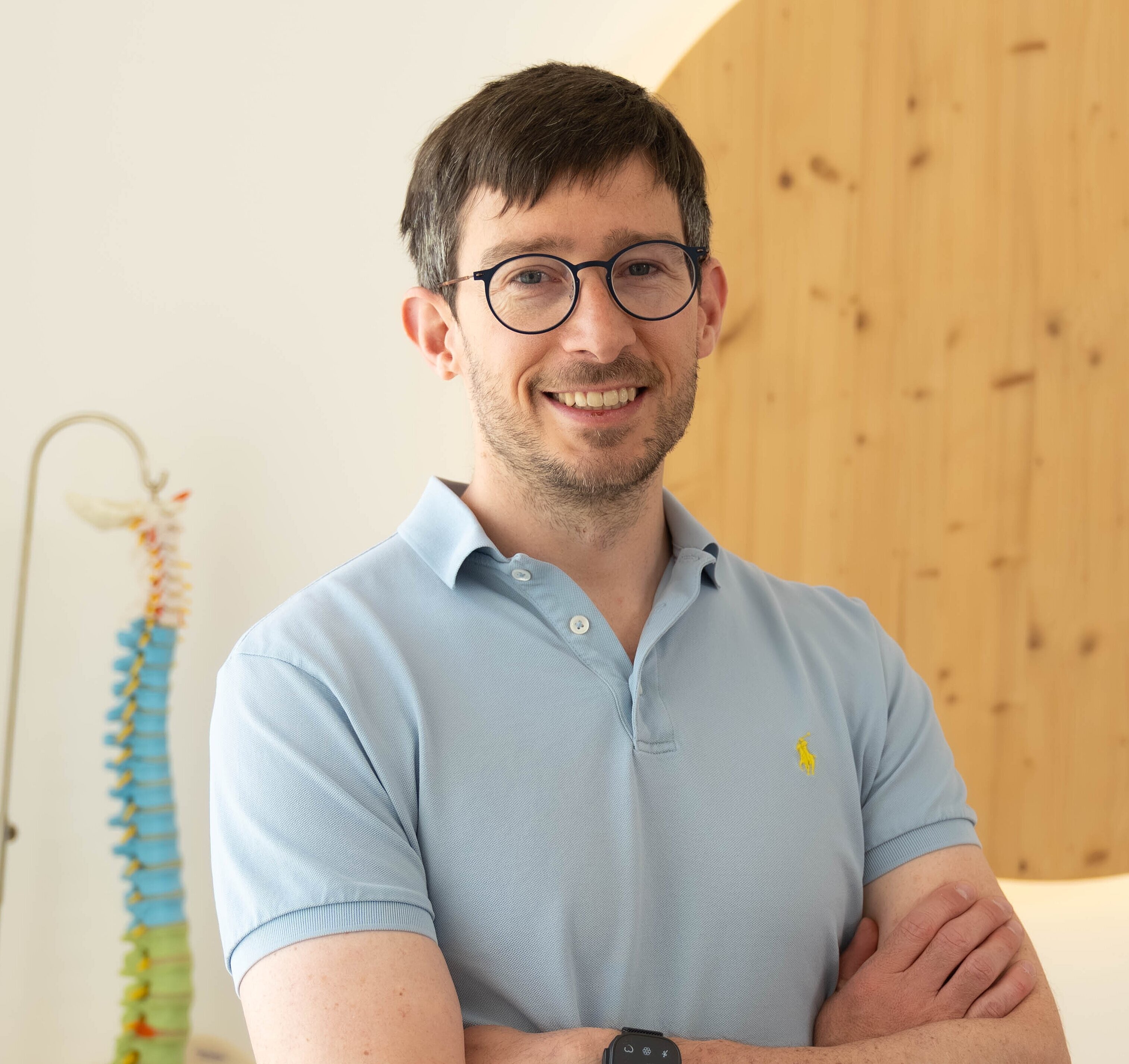 Man with glasses wearing a blue polo shirt standing with arms crossed in front of a model spinep