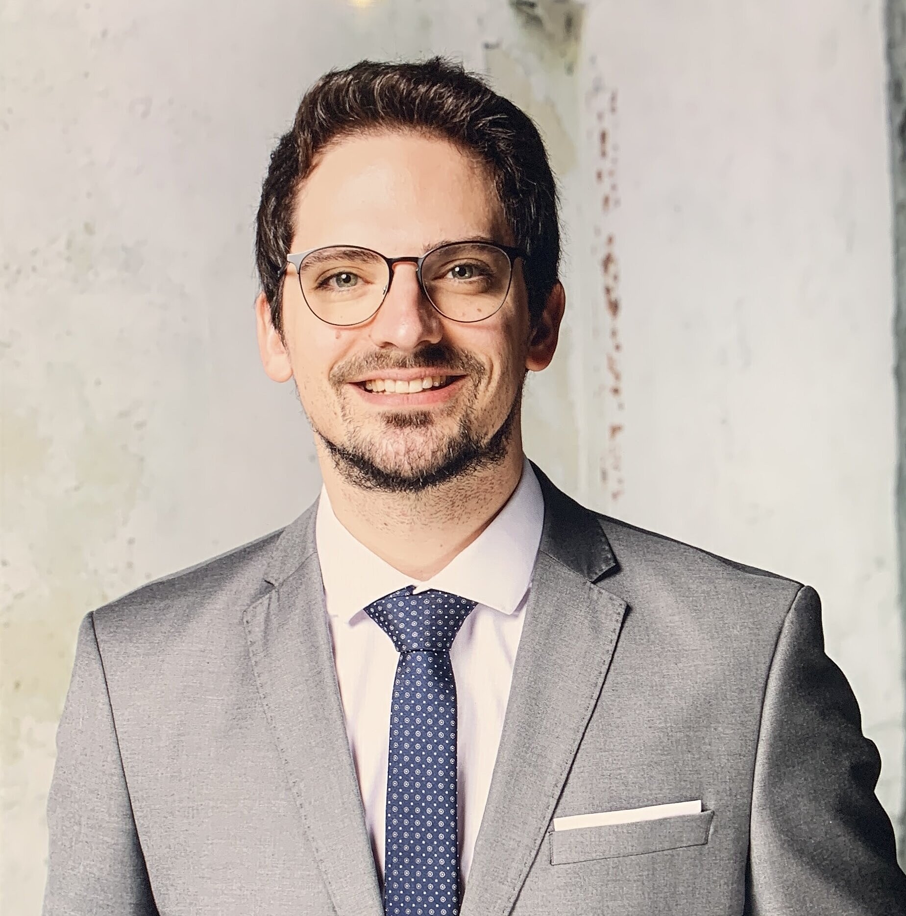 Mann mit Brille in grauem Anzug.