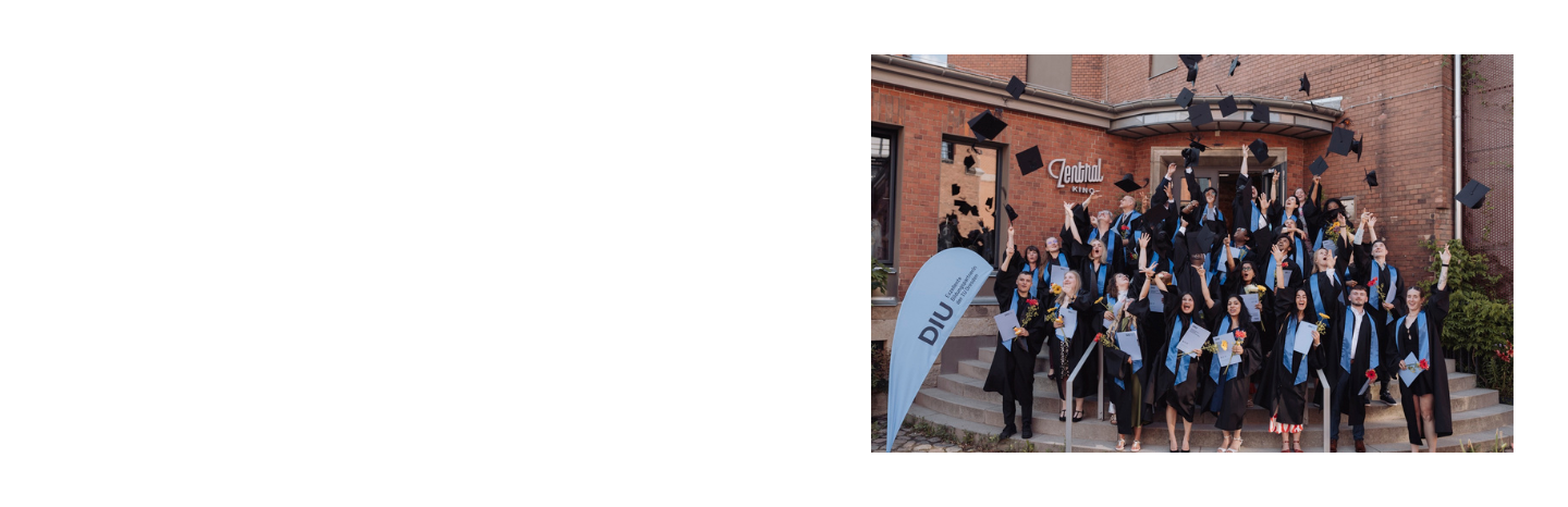 Group of graduates in caps and gowns throwing their caps in the air outside a brick building.