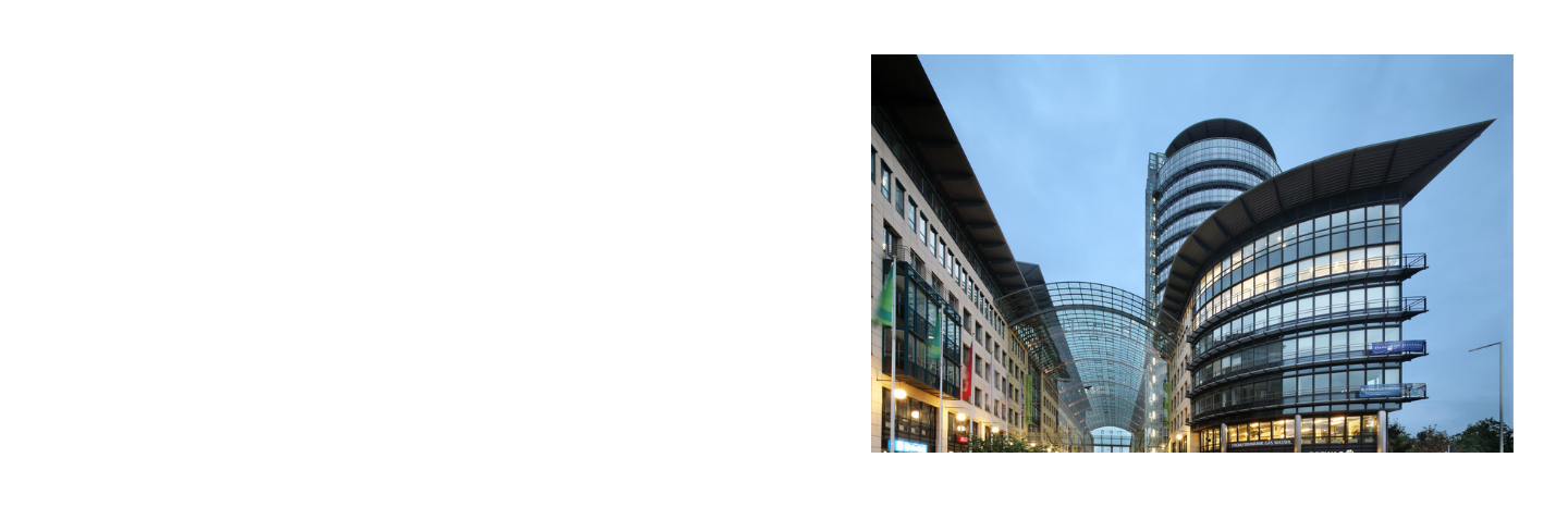Blick in eine moderne Straßenpassage mit Glasdach zwischen zwei mehrstöckigen Gebäuden mit vielen Fenstern