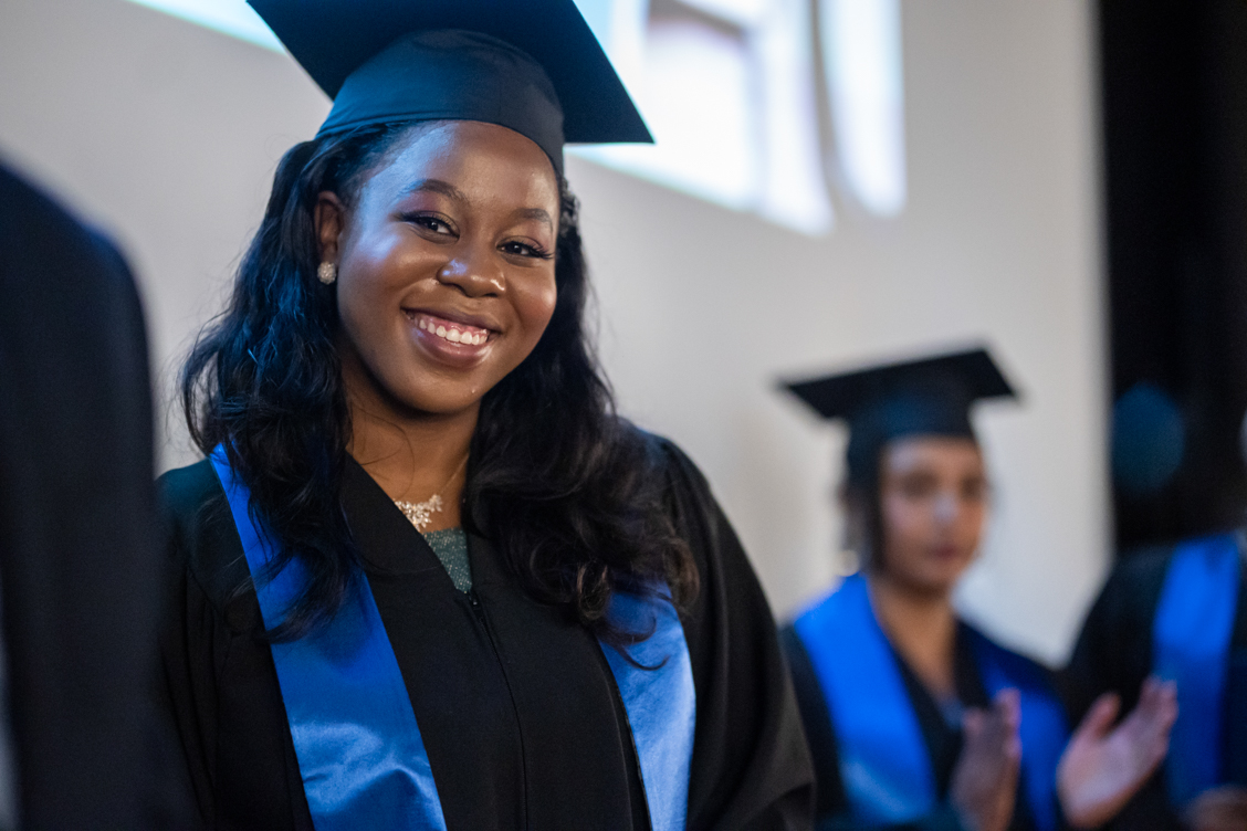 Smiling woman in graduation gown and cap with blue stole in a ceremony setting
